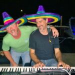 Two men having fun playing keyboard with sombreros on